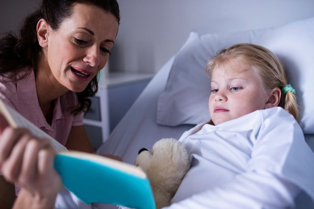 Girl on a bed reading book with her mother in hospital