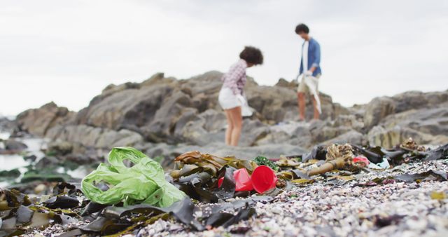 Two people collecting garbage on a rocky beach, highlighting environmental conservation and volunteer efforts. Great for promoting community service initiatives, environmental awareness campaigns, and marine preservation efforts.
