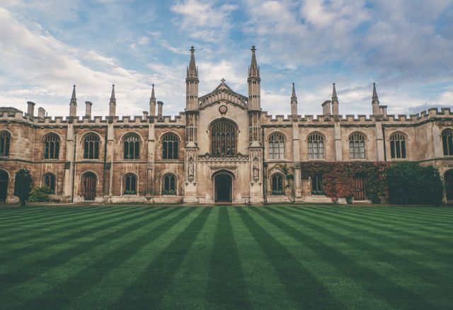 This scene captures a splendid example of Gothic architecture, showcasing a college or university building. The meticulously manicured lawn and classic design of the structure contribute to a sense of academic excellence. Ideal for use in educational materials, travel brochures, history presentations, architecture studies, and promotional content for academic institutions.