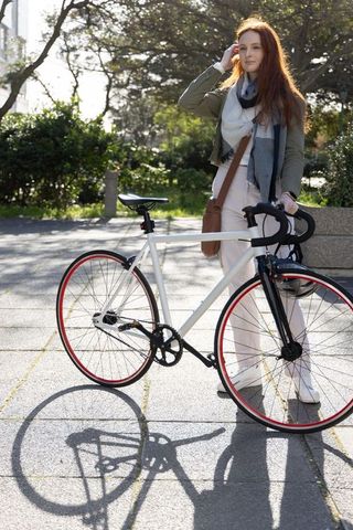 Redhead woman holding bicycle and touching hair in sunlit urban plaza with scarf