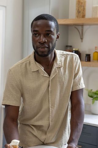 African american man leaning on kitchen counter holding mug, contemplative natural-light portrait