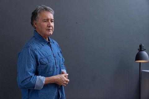 Senior man in denim shirt standing by modern black desk lamp