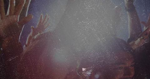 Diverse concert crowd raising hands toward pulsing spotlight with grainy haze