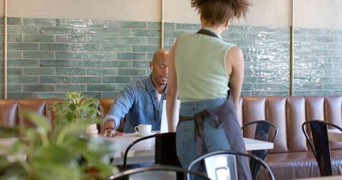 African american female server talking with seated customer in modern cafe interior