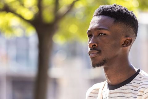 Young african american man gazing thoughtfully outdoors with sunlit bokeh urban background