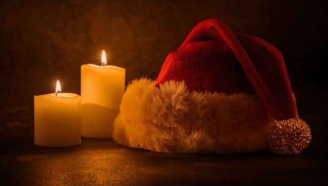 Santa hat and candles casting warm golden glow on dark tabletop holiday still life