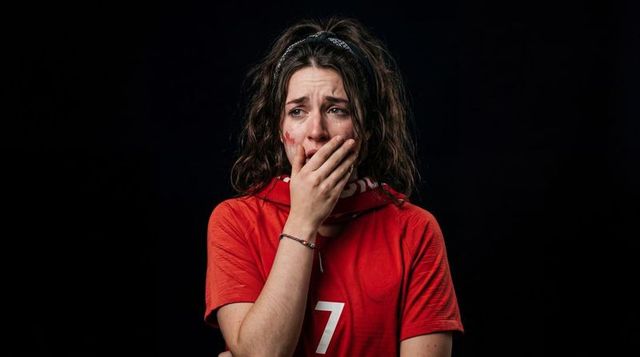 Tearful football fan reacting to loss crying and covering mouth wearing red 7 jersey