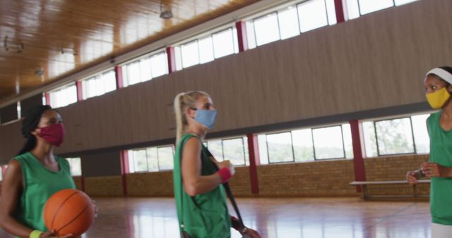 Diverse female basketball team greeting with elbows, wearing face masks. basketball, sports training at an indoor court during coronavirus covid 19 pandemic.