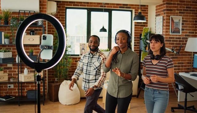 Diverse creators streaming collaborative content in bright loft studio with ring light