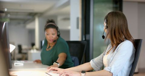 Multiracial customer service agents collaborating at open office desks with headsets