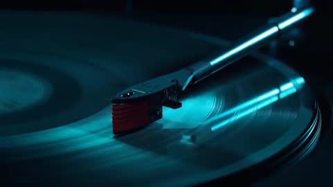 Red stylus tracking inward on spinning vinyl record with teal glow and reflective grooves