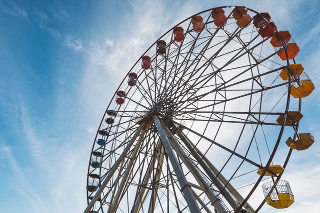 A colorful Ferris wheel towering against a vibrant blue sky with scattered clouds. Perfect for themes related to amusement parks, festive scenes, outdoor fun, and fairgrounds. Ideal for advertisements, marketing materials promoting entertainment venues, or backgrounds for websites and social media posts about leisure activities.
