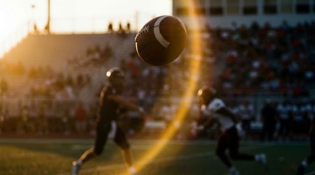 Floating football capturing golden sunset lens flare over stadium crowd