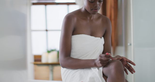 African american attractive woman doing a manicure in bathroom. beauty, pampering, home spa and wellbeing concept.