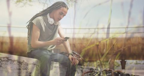 Man with Dreadlocks Relaxing Outdoors Using Smartphone
