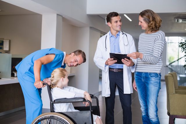 Doctor discussing medical report with mother while nurse assists child in wheelchair in hospital corridor. Ideal for healthcare, medical consultation, patient care, and family health-related content.