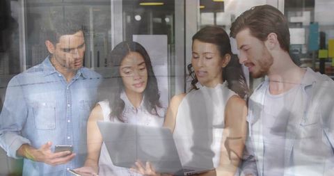 Diverse team engaged in office collaboration using laptop and smartphone