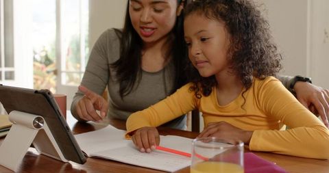 Mother helping daughter with homework using tablet on dining table together
