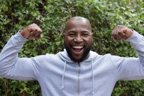 Joyful african american man flexing muscles while smiling in backyard wearing gray hoodie