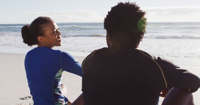 African american couple talking and sitting on the beach. holiday and healthy outdoor leisure time by the sea.