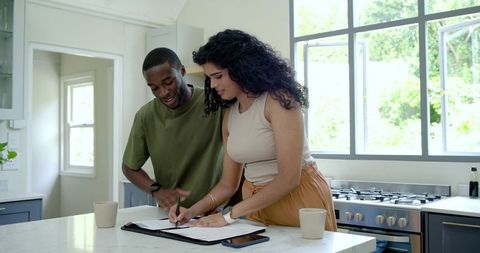 Couple signing mortgage documents on marble kitchen island, reviewing home loan contract