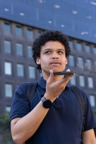 African american commuter speaking into smartphone near office tower using voice assistant