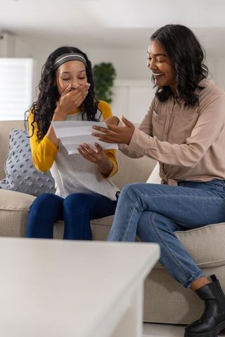 Mother and teen daughter reacting with surprise and joy to letter on cozy living room couch