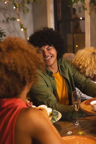 Friends laughing around dinner table sharing pizza and desserts in cozy indoor gathering