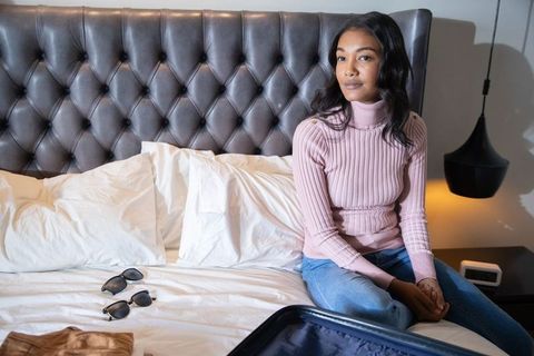 Woman Preparing for Trip Seated on Bed with Open Suitcase