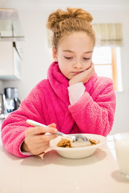 Sad girl in bathrobe having breakfast in kitchen at home