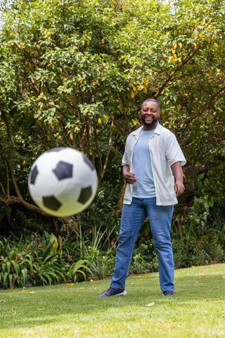 African man smiling and watching soccer ball in sunny backyard garden, casual lifestyle