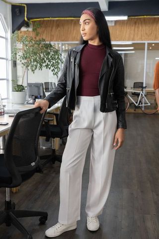 Asian woman standing in leather jacket resting hand on chair in modern coworking space