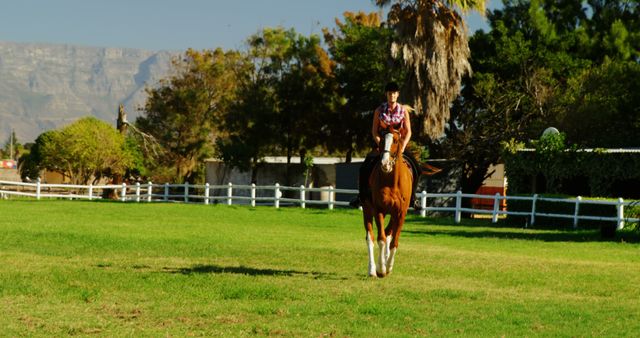 A young Caucasian woman enjoys horseback riding in a sunny outdoor setting, with copy space. She appears confident and relaxed as she trots across the grassy field.