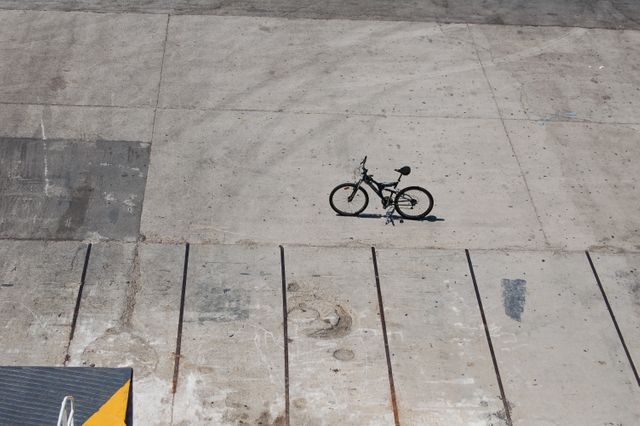 Minimalist single bicycle on large concrete surface with shadow casting, perfect for themes of solitude, simplicity, and urban lifestyle. Can be used in blogs about urban exploration, travel, sustainability, or as background for design projects and presentations emphasizing empty spaces and loneliness.