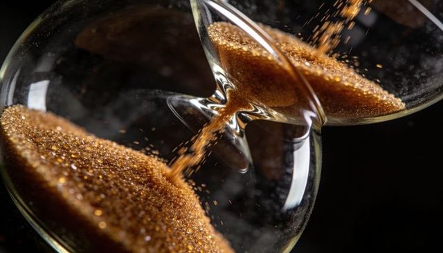 Macro hourglass pouring golden sand close-up showing glittering granules and flowing time