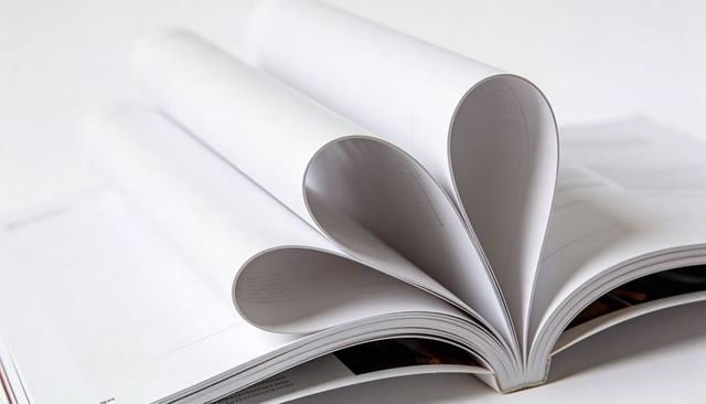 Three heart shapes forming from curled magazine pages close-up on white background romantic concept