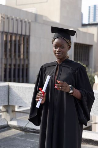 African american graduate holding diploma on urban rooftop wearing cap and gown