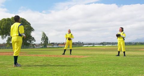 Female softball teammates in uniforms holding gloves on field
