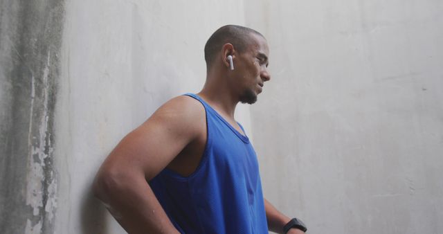 Sweaty biracial sports man wearing blue tshirt and earphones in city. Sport, active lifestyle and technology.