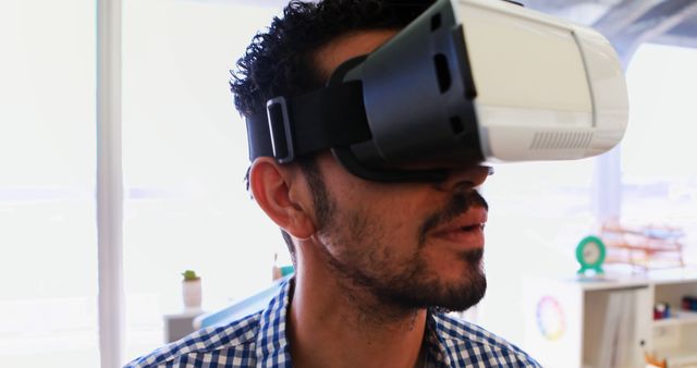 Man exploring virtual reality while wearing VR headset in bright, modern office. This image is useful for illustrating concepts related to technology, innovation, virtual reality immersion, modern workplace, and tech-savvy environments.