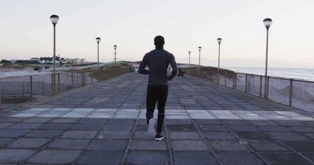 Back view of african american man exercising outdoors, running by seaside. fitness, active and healthy lifestyle concept.