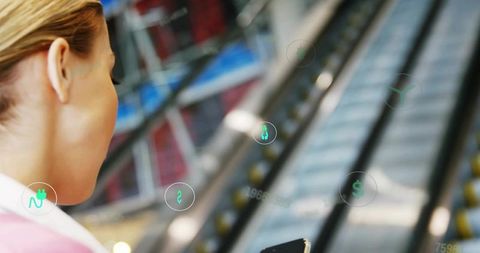 Woman holding smartphone viewing augmented reality retail icons above mall escalator