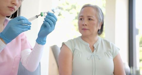 Nurse preparing syringe for vaccination as senior woman waits