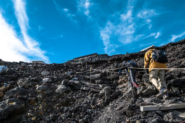 Hikers Climbing Rocky Trail Towards Mountain Hut Under Bright Blue Sky - Download Free Stock Images Pikwizard.com