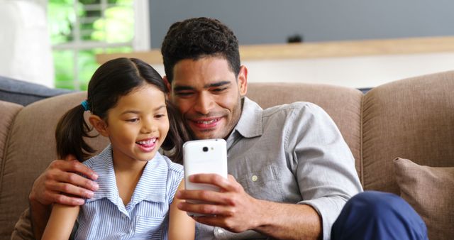 Father and Daughter Enjoying Time Together Using Smartphone on Couch - Download Free Stock Images Pikwizard.com