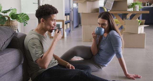 Couple taking a break with coffee surrounded by unpacked boxes in their new home. Perfect for content related to moving, home ownership, new beginnings, lifestyle, relationships, and casual home moments.