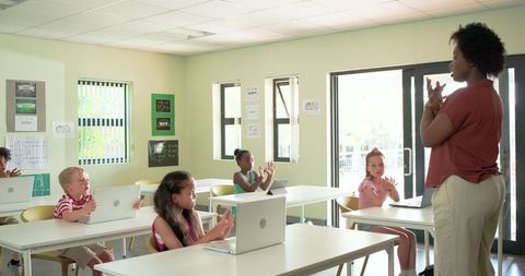 African American Teacher Demonstrating Hand Gestures to Elementary Students Using Laptops