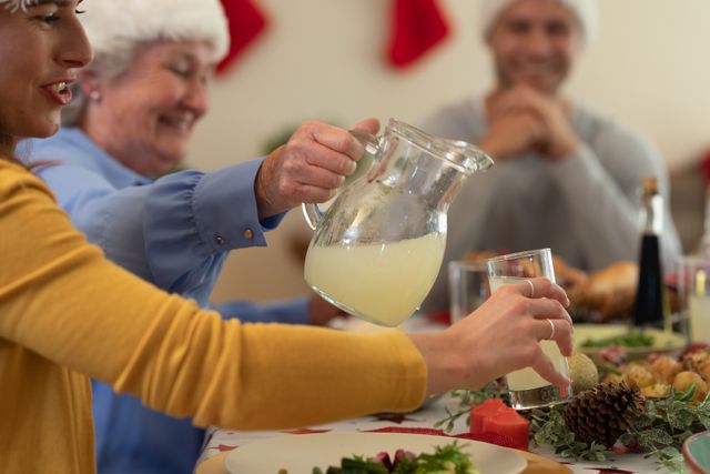 Caucasian family enjoying Christmas dinner together. Elderly woman pouring a drink for the woman beside her while a man smiles in the background. Ideal for holiday celebration themes, family gatherings, and festive season promotions.
