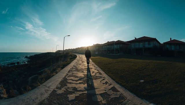 Walking alone on cracked coastal promenade at sunset casting long shadow