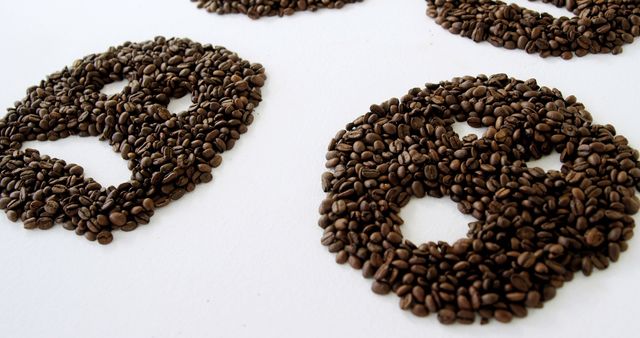 Coffee beans are arranged in circular patterns on a white surface, creating an artistic and textured appearance. This creative display showcases the versatility of coffee beans beyond their traditional use in brewing.